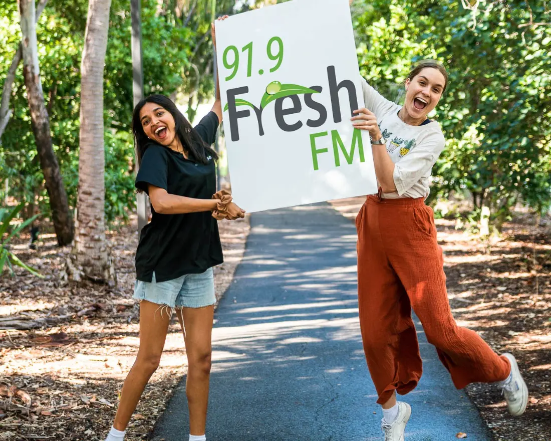 Two YWAM volunteers holding a 91.9 Fresh FM sign